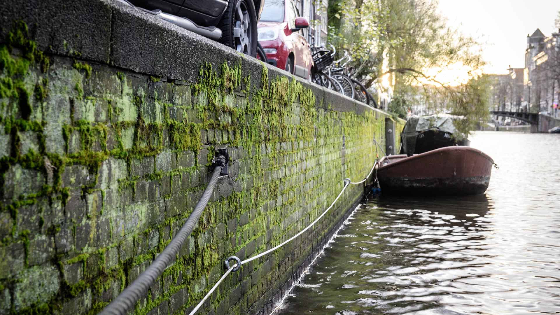 Kademuren langs gracht in Amsterdam met bootje en geparkeerde fietsen en auto's