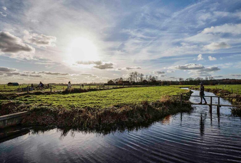 Weiland met bruggetje en wandelaar met water, blauwe lucht en zonnetje in Noord Holland