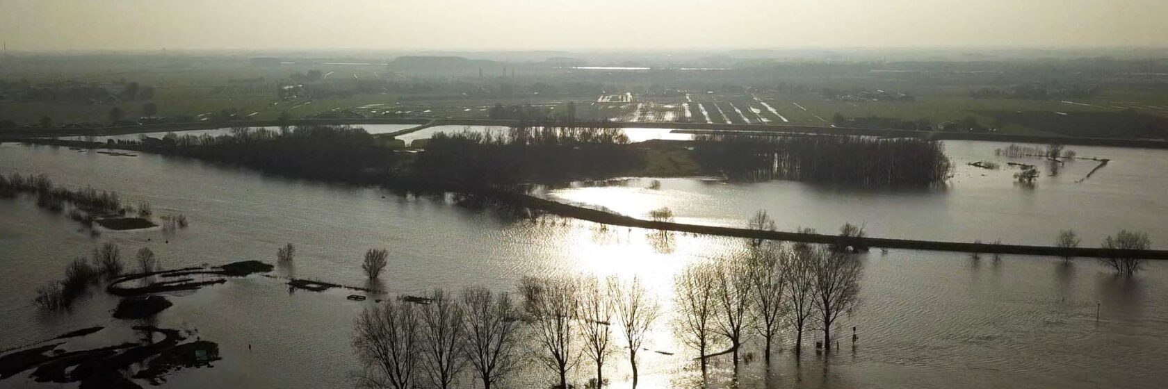 Hoogwater bij uiterwaarde met ondergaande zon