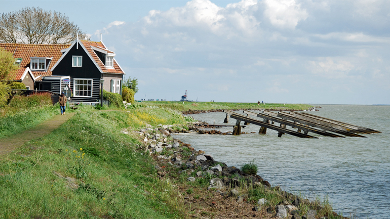 Zwart houten huis met rode dakpannen aan rand van water