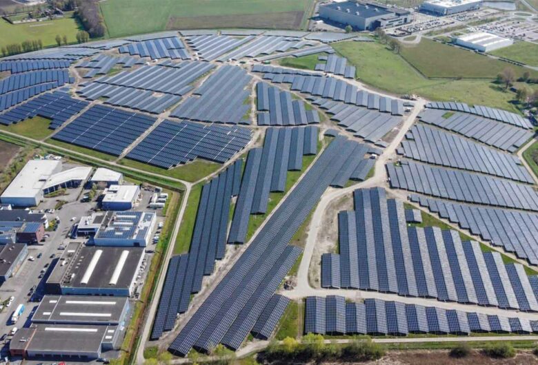 Luchtfoto met duizenden zonnepanelen op een berg met groen en gebouwen erom heen