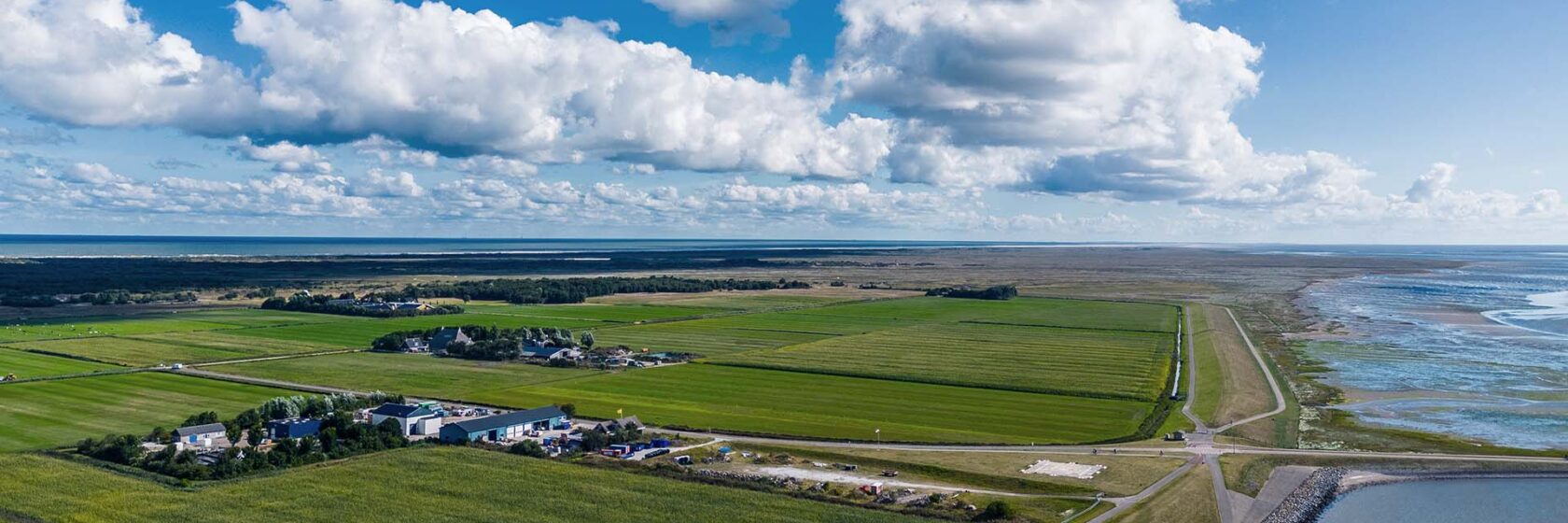 Luchtfoto van de kust met dijkversterking. Groen weilanden en blauwe wolkenlucht.