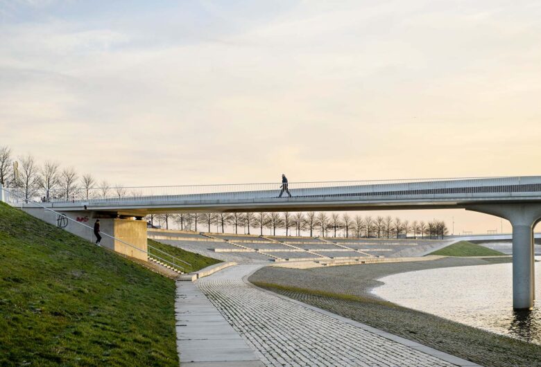 Wandelaar over een brug die over de Waal en de kade gaat tegen een lucht met avondrood.
