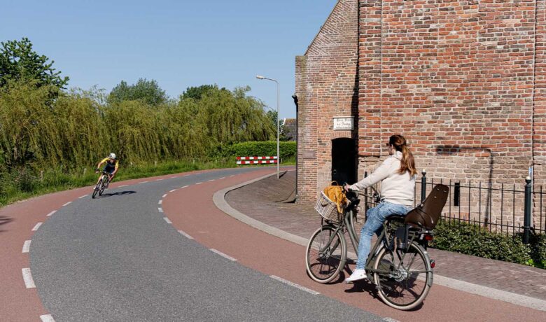 Fietsende vrouw op rood fietspad met gebouw op achtergrond en tegemoetkomende wielrenner