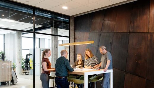 Samenwerking van meerdere collega's rondom een staande tafel. Ze kijken naar een technische bouwtekening en overleggen met elkaar.