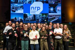 Groep mensen ontvangt NRP Gulden Feniks awards, poseren met bloemen en trofeeën voor presentatiescherm.