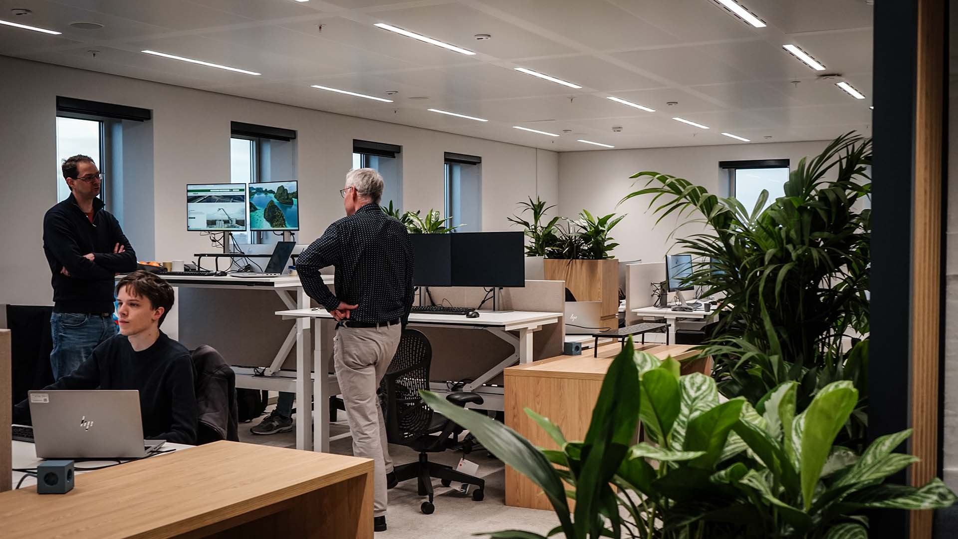 Licht kantoor met werkende mensen en computer met groene planten rechts