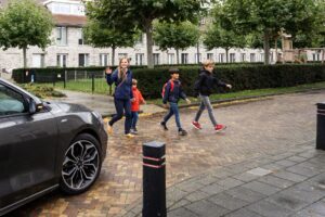 Weg met auto en overstekende kinderen en vrouw met groene bomen op achtergrond