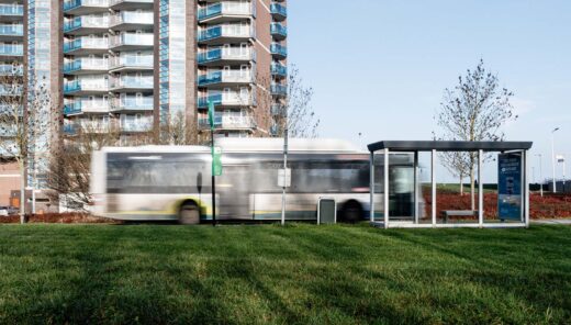 Bus met bushokje rechts en flatgebouw op achtergrond