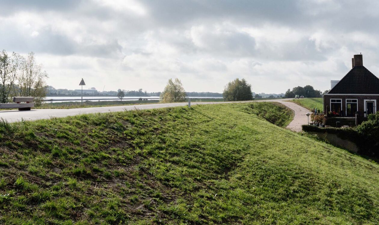 Groene dijk met weg erop, links rivier, rechts huis bij Tiel-Waardenburg