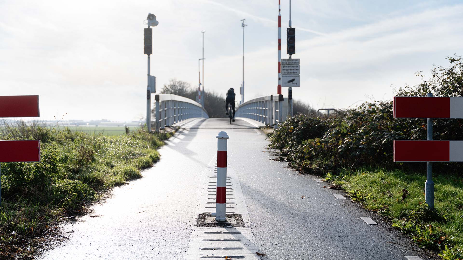 Vooraanzicht fietsbrug met fietser met stoplichten en slagbomen.