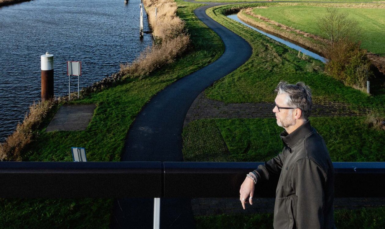 Man, Berry Veenhof, op fietsbrug uitkijkend over groen landschap en water.
