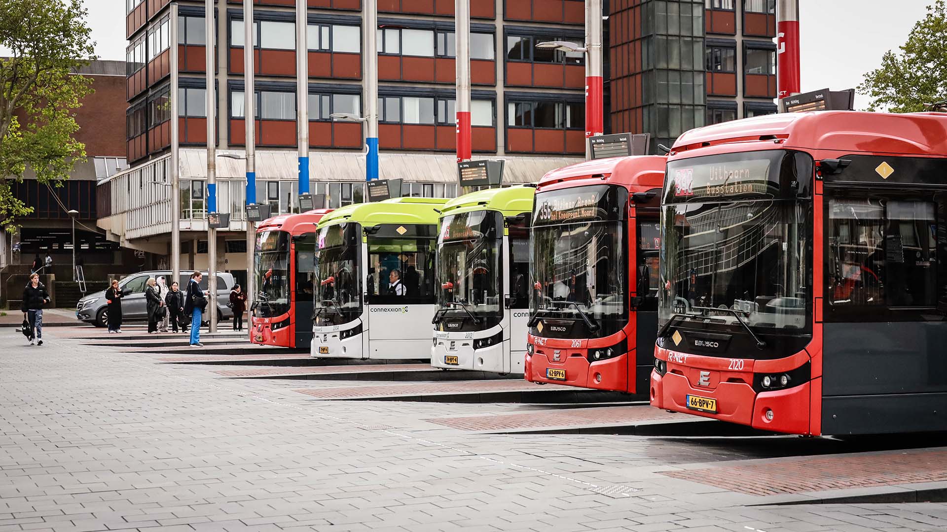 drie rode bussen en drie wit gele bussen op een station in stedelijke omgeving.