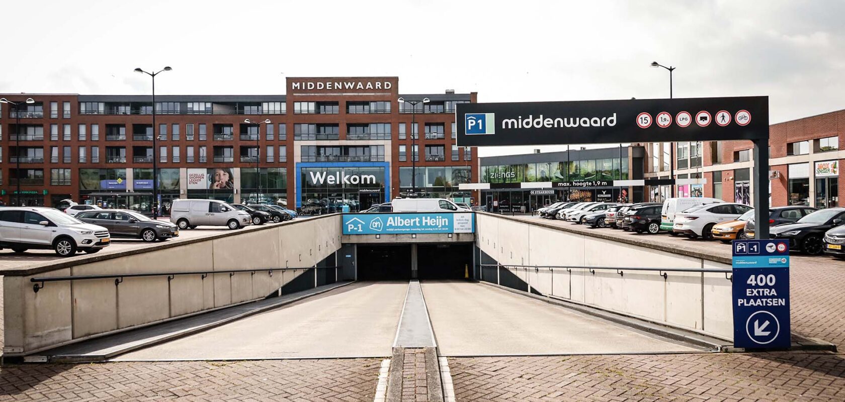 Ingang parkeergarage midden in parkeerdek met meerlaagse gebouwen op de achtergrond