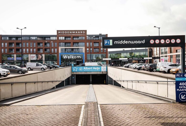 Ingang parkeergarage midden in parkeerdek met meerlaagse gebouwen op de achtergrond