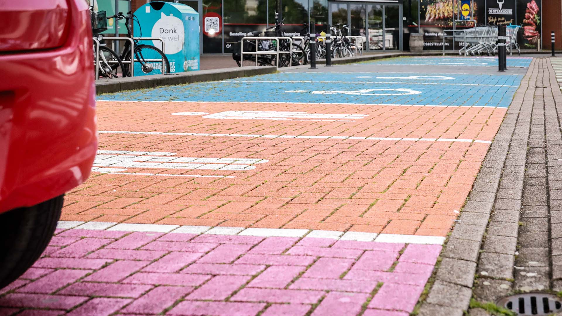 Roze, oranje en blauwe parkeervakken met iconen voor de verschillende doelgroepen op parkeerterrein.