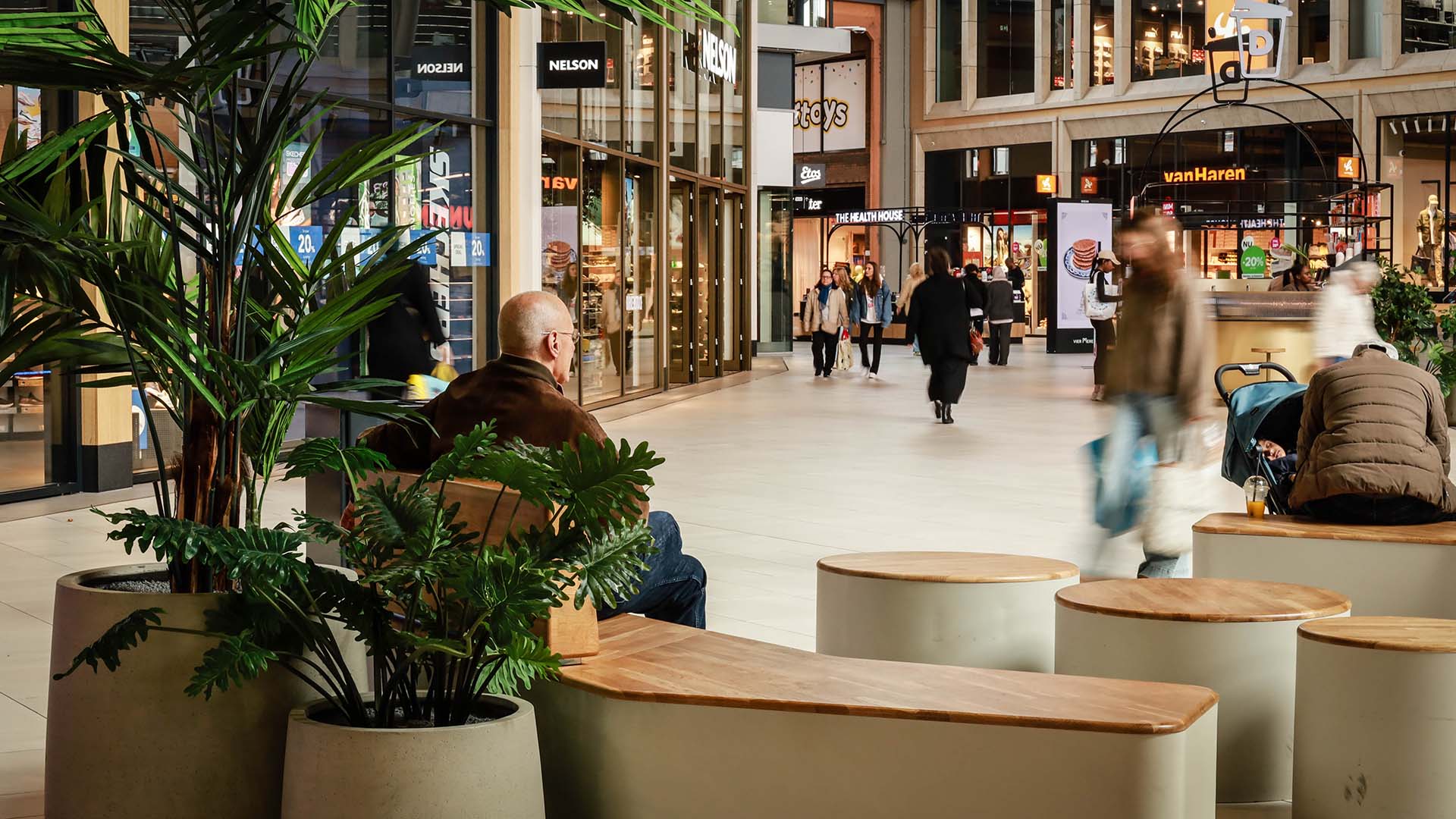 Binnenfoto van een winkelcentrum met bezoekers op bankjes en planten