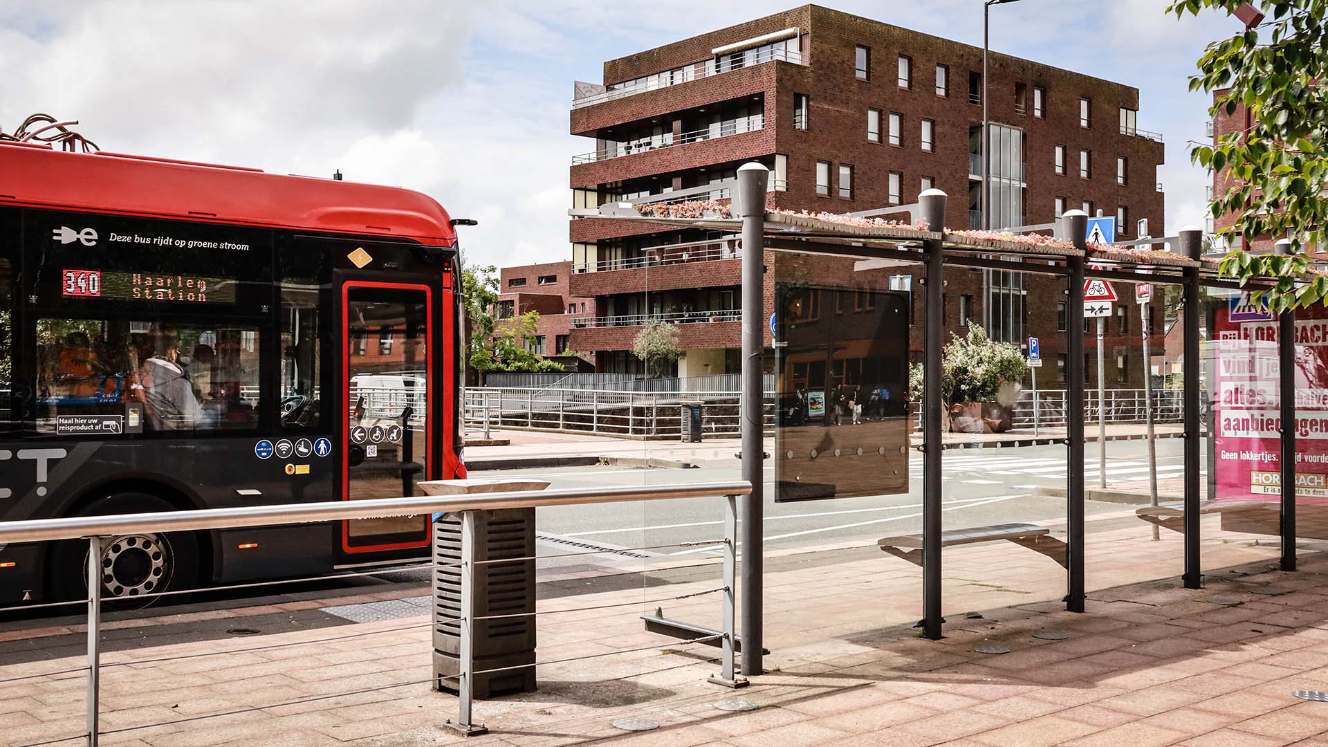 Tramhalte met rode tram en appartementencomplex op de achtergrond.
