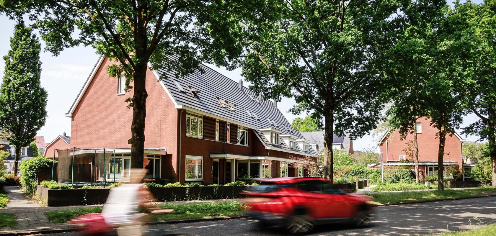 Huizen langs weg met bomen met voorbijgaande fietser en rode auto