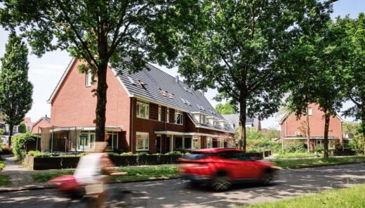 Huizen langs weg met bomen met voorbijgaande fietser en rode auto