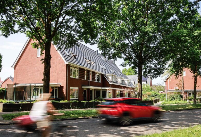 Huizen langs weg met bomen met voorbijgaande fietser en rode auto