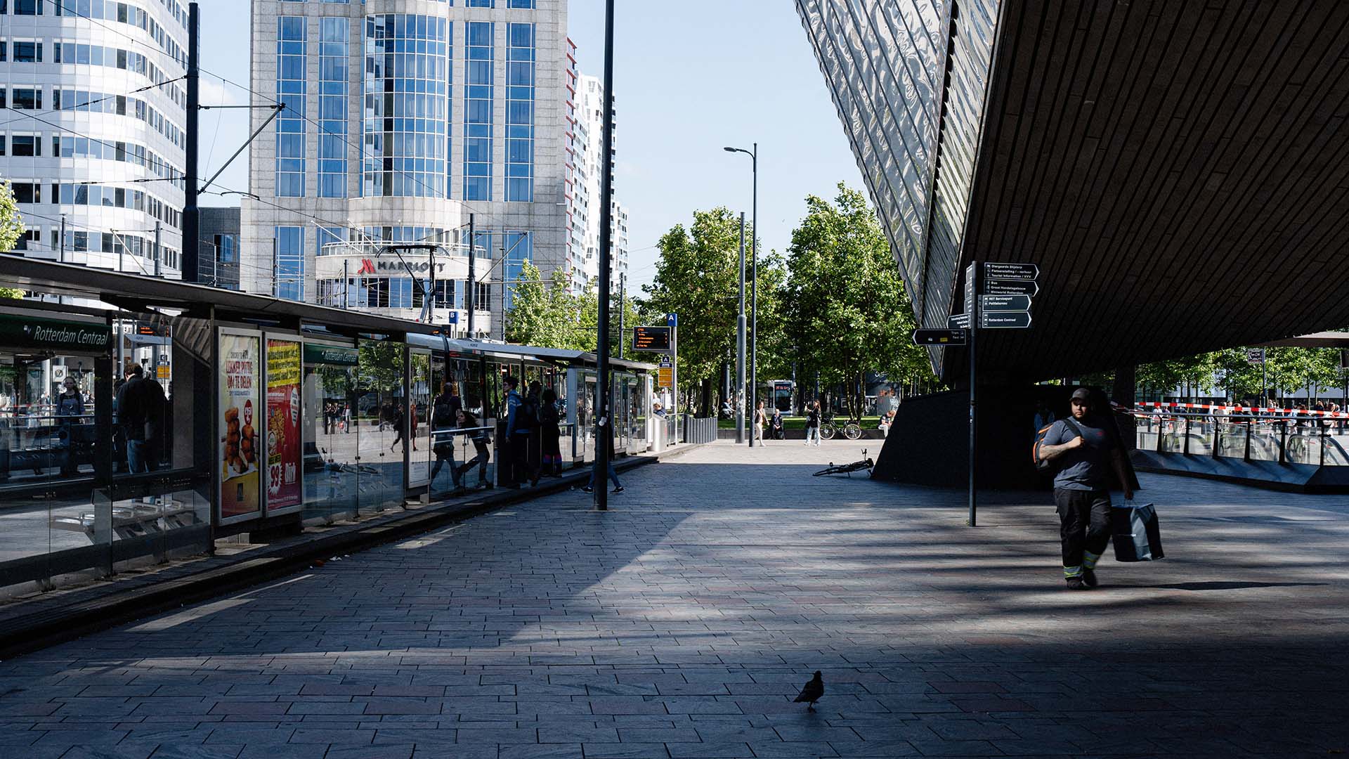 Tram bij station met passagier op perron. Hoge gebouwen en groene bomen op achtergrond