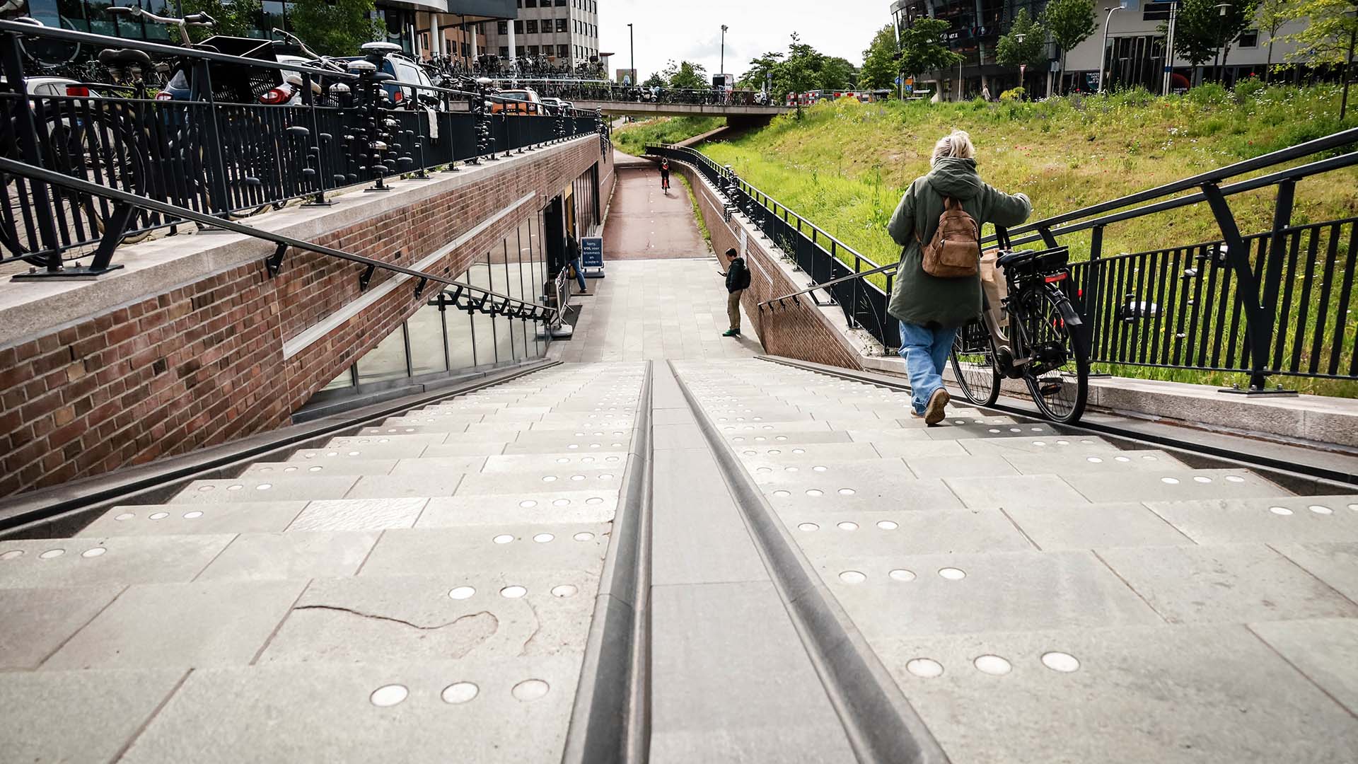 Voetganger met fiets aan de hand op fietstrap op een station