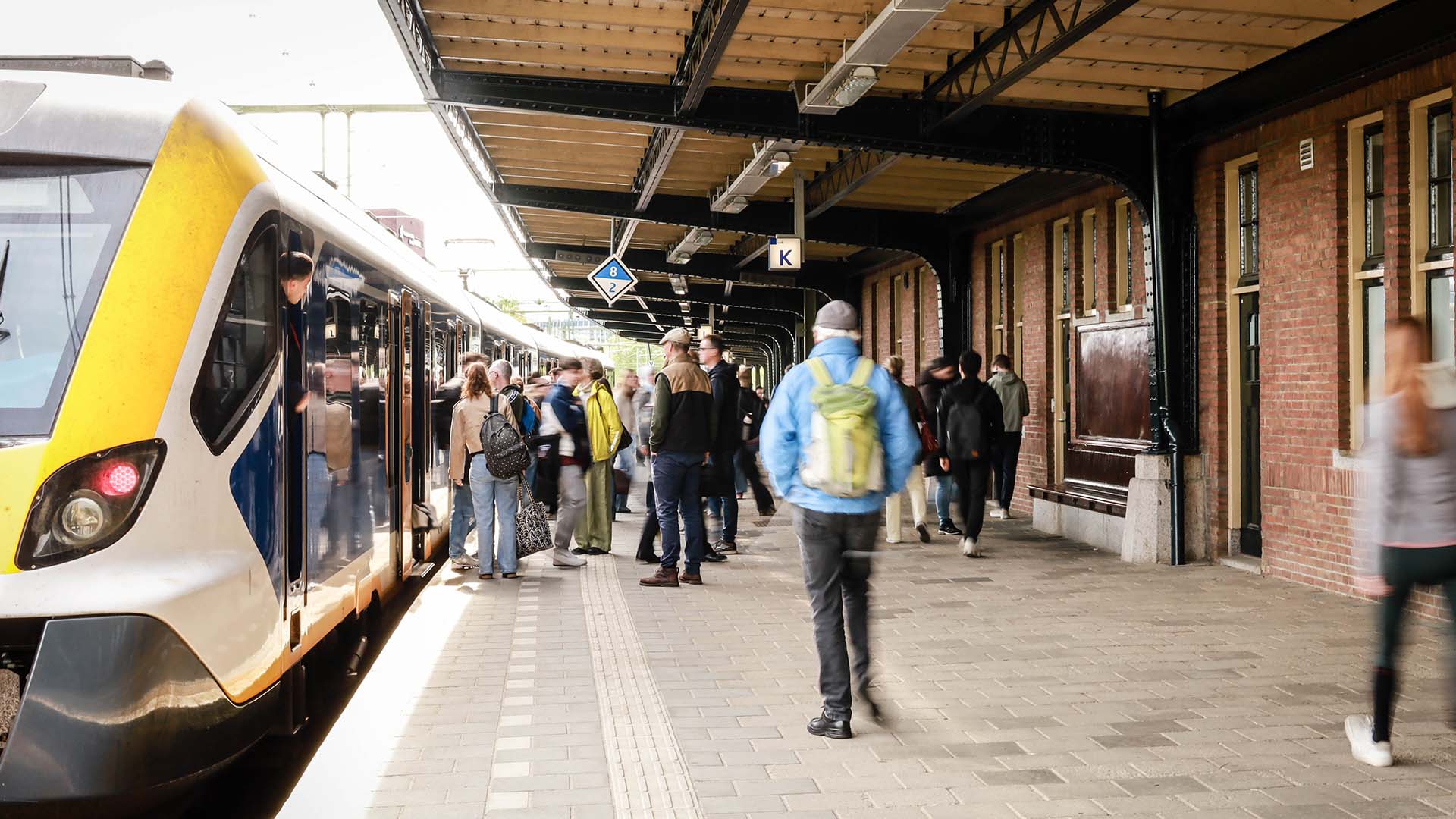 Overkapt treinperron met vele passagiers die in en uitstappen in wachtende trein