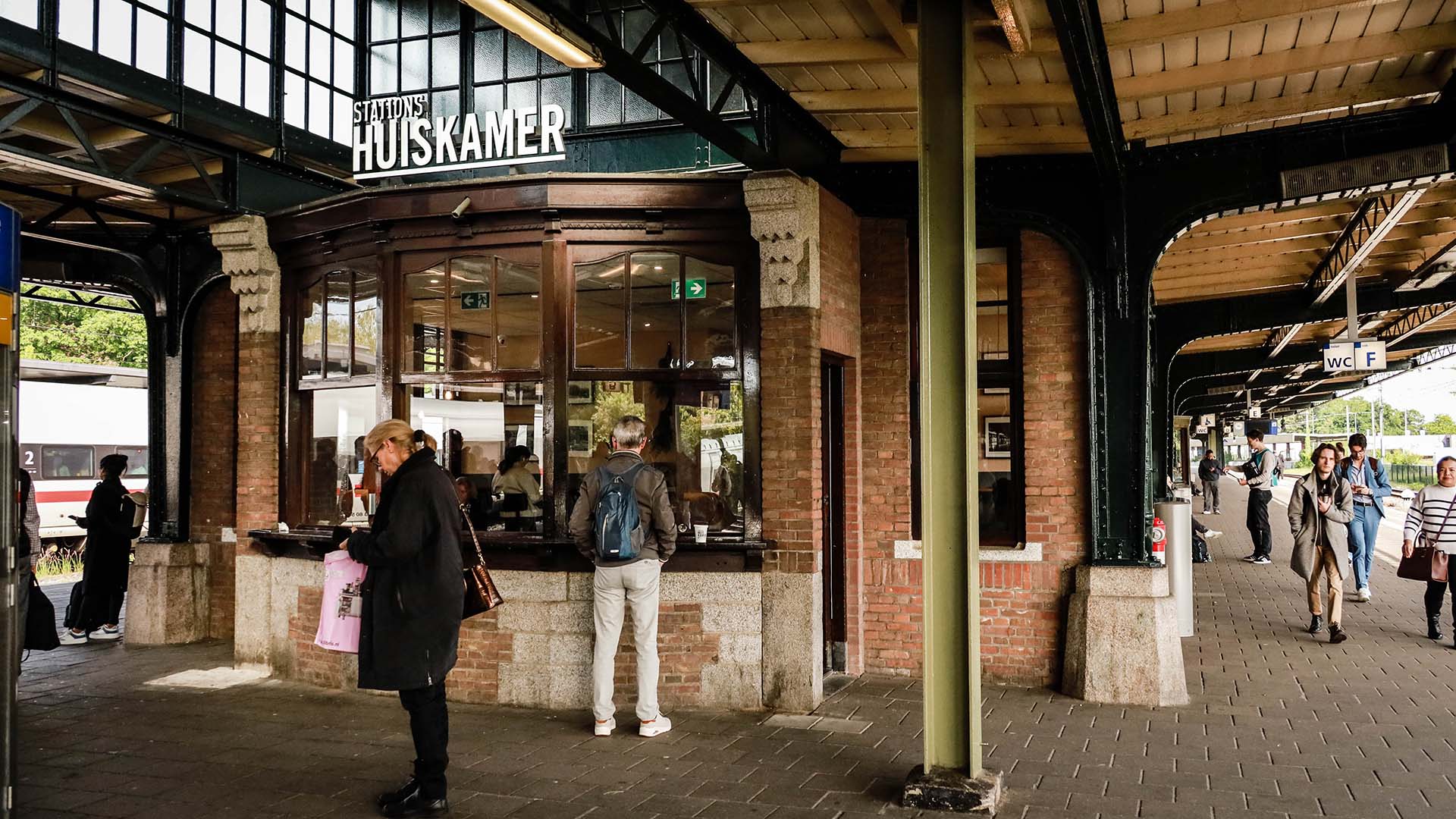 Mensen die wat kopen op overdekt station bij de kiosk met perron op achtergrond