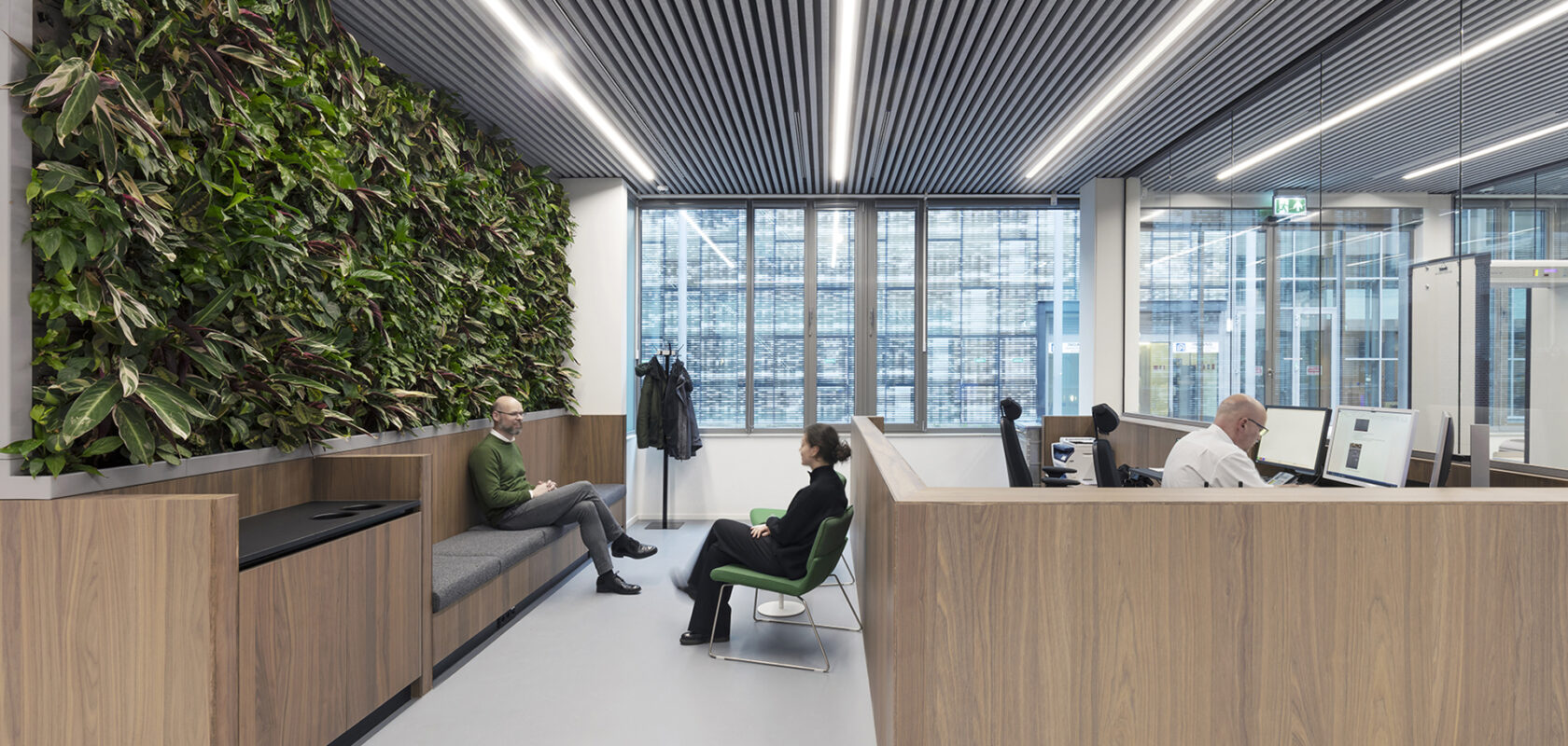 Binnenfoto van modern kantoor met groene plantenwand en mensen achter computer.