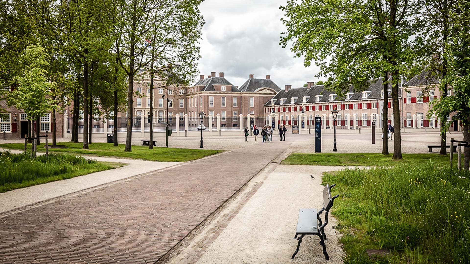 Oprijlaan met groene bomen naar monumentaal gebouw met plein ervoor