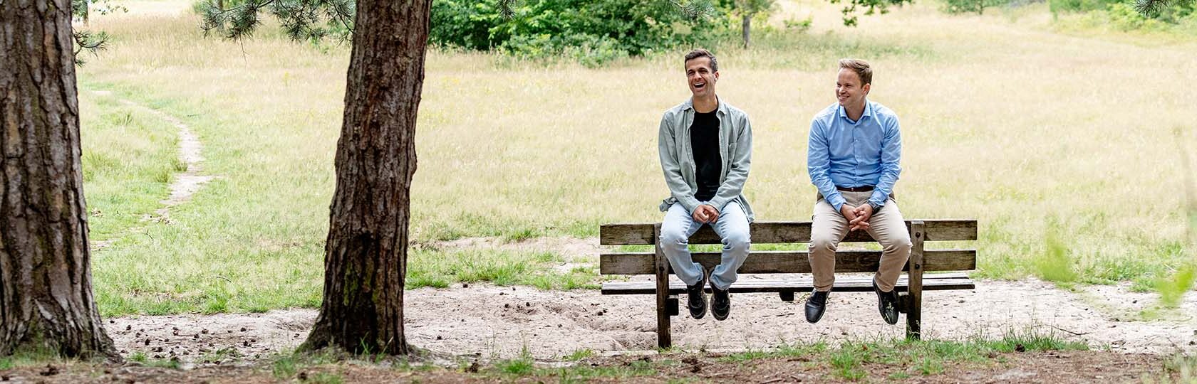 Twee mannen op een bankje voor een weiland en naast bomen
