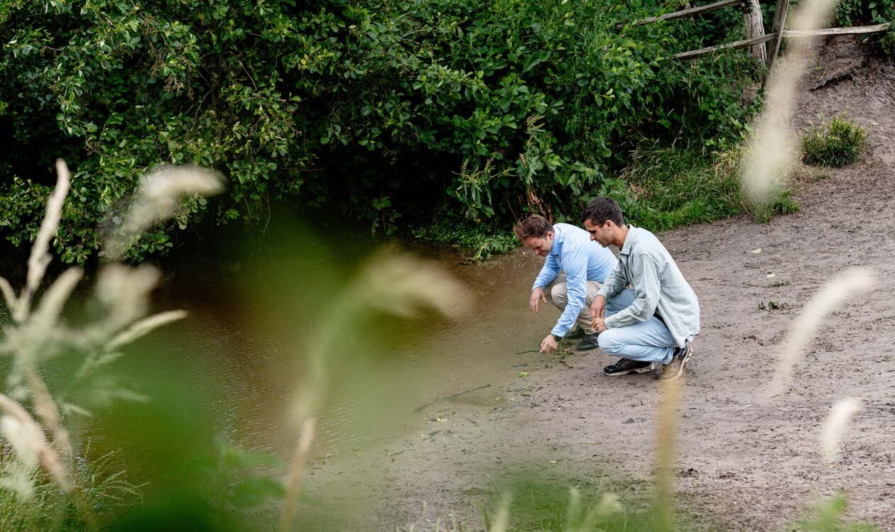 Twee mannen bij de oever van een meertje kijkend naar water